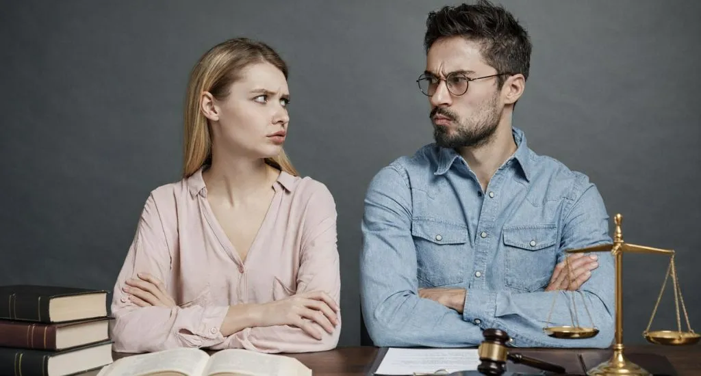 Paar sitzt sich angespannt gegenüber mit Dokumenten zur Scheidung und juristischen Unterlagen auf dem Tisch